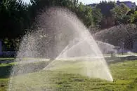 Water sprinkler system spraying lush green grass in a sunny outdoor setting, ideal for lawn care illustrations.